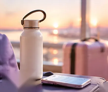 Water bottle and suitcase by a sunset window